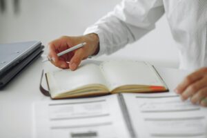 Close-up of a businessman writing notes in a diary at a modern office desk.